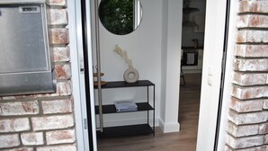 A doorway leading to a room with a brick wall, a round mirror, a black console table with a vase, and a shelf with a book. - Beautiful vacation apartment near Pietzmoor (Schneverdingen)