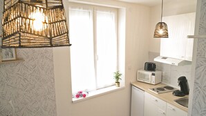 Eine kleine Küche mit Fenster, einer Mikrowelle, einer Kaffeemaschine und einer Pendelleuchte.