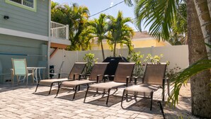 Une terrasse avec quatre chaises longues, un barbecue et une petite table.
