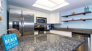 Uma cozinha moderna com eletrodomésticos de aço inoxidável, bancadas de granito e um claraboia.