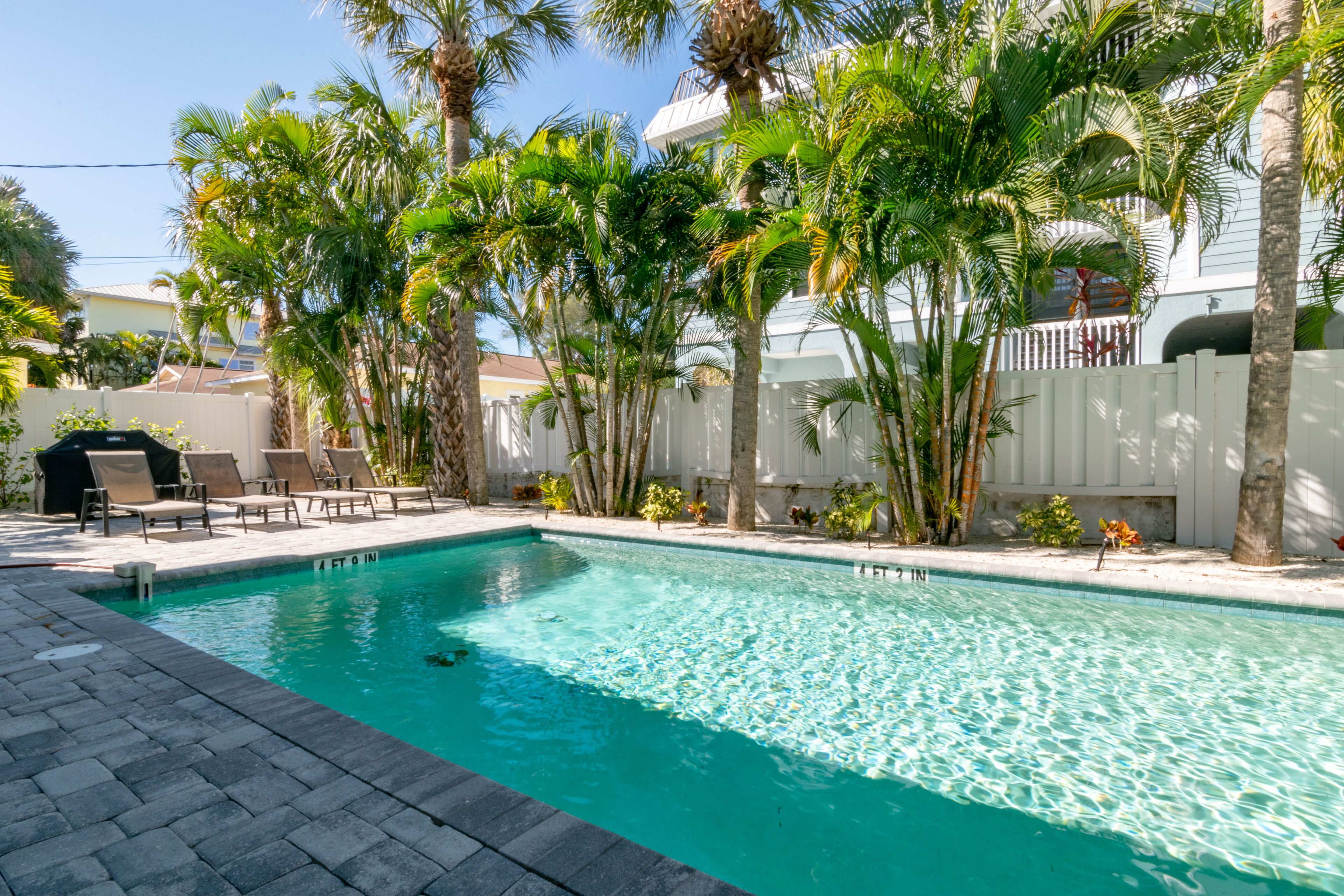 A swimming pool with clear blue water, surrounded by palm trees and lounge chairs.