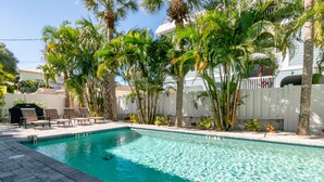 Une piscine à l’eau d’un bleu cristallin, entourée de palmiers et de chaises longues.