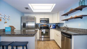 Une cuisine compacte dotée d’un îlot central, d’appareils électroménagers en acier inoxydable et d’un puits de lumière.