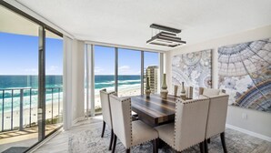 A dining area with a view of the ocean, a large window, and a modern chandelier. - Remodeled! Beachfront Wraparound Balcony Edgewater (Panama City Beach)