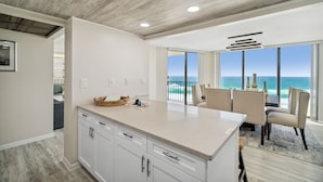 A modern kitchen with a large island, white cabinetry, and a view of the ocean. - Remodeled! Beachfront Wraparound Balcony Edgewater (Panama City Beach)