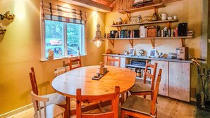 Una cocina acogedora con una mesa redonda de madera, sillas y estantes con diversos utensilios de cocina.