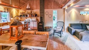 Interior acogedor de una cabaña con una mesa de comedor de madera, una chimenea, un sofá cómodo y una estantería llena de libros y objetos decorativos.