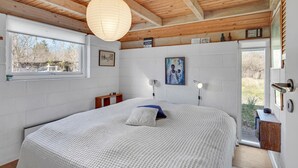 A bedroom with a large bed, a wooden ceiling, a window, and artwork on the walls.