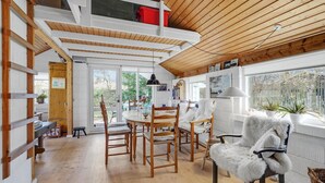A cozy dining area with wooden chairs and a table, a white furry chair, and a window with plants.