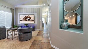 Un salon moderne avec une grande télévision, des canapés gris, une table basse et un miroir décoratif.
