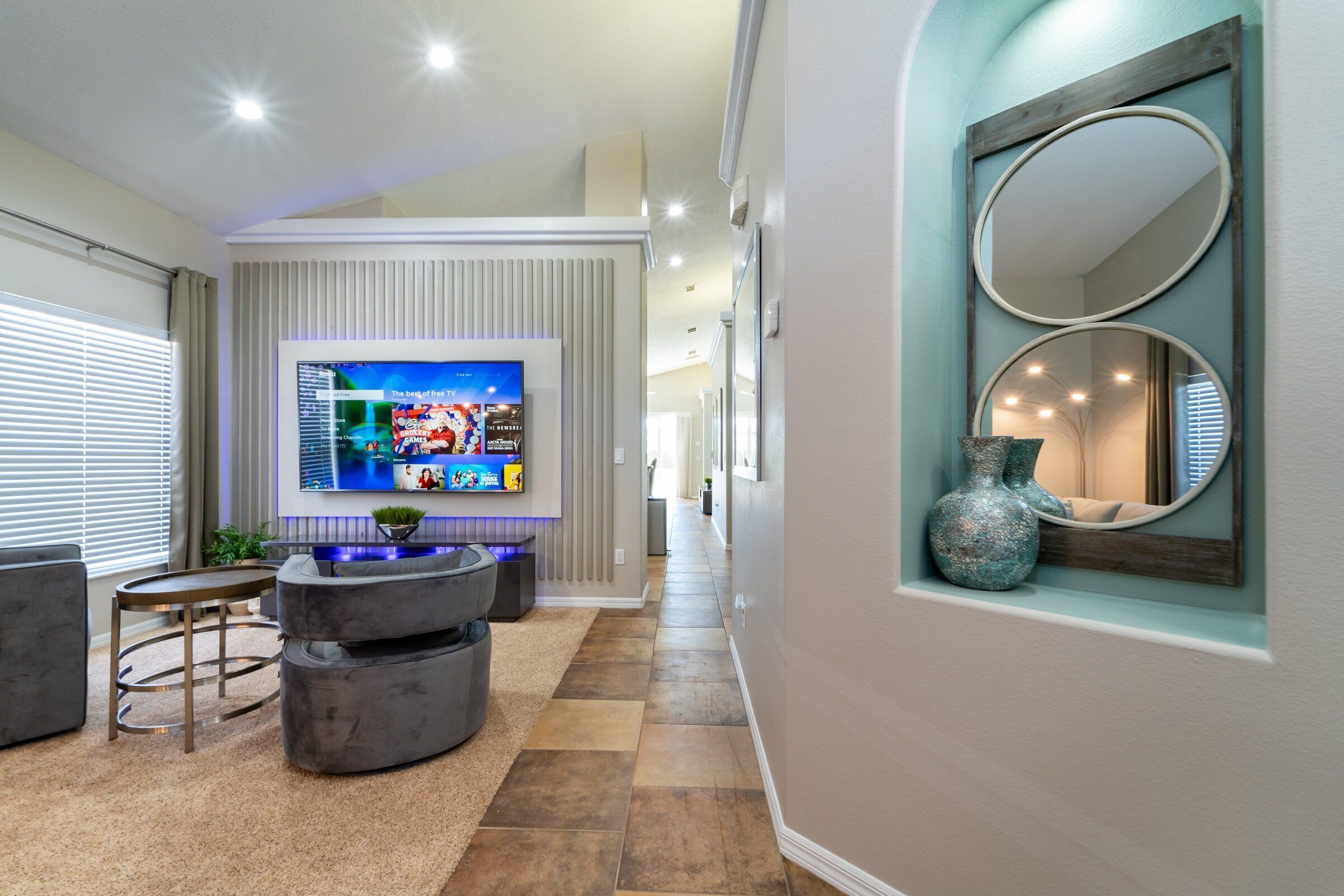 A modern living room with a flat-screen TV, a round coffee table, and a decorative mirror.