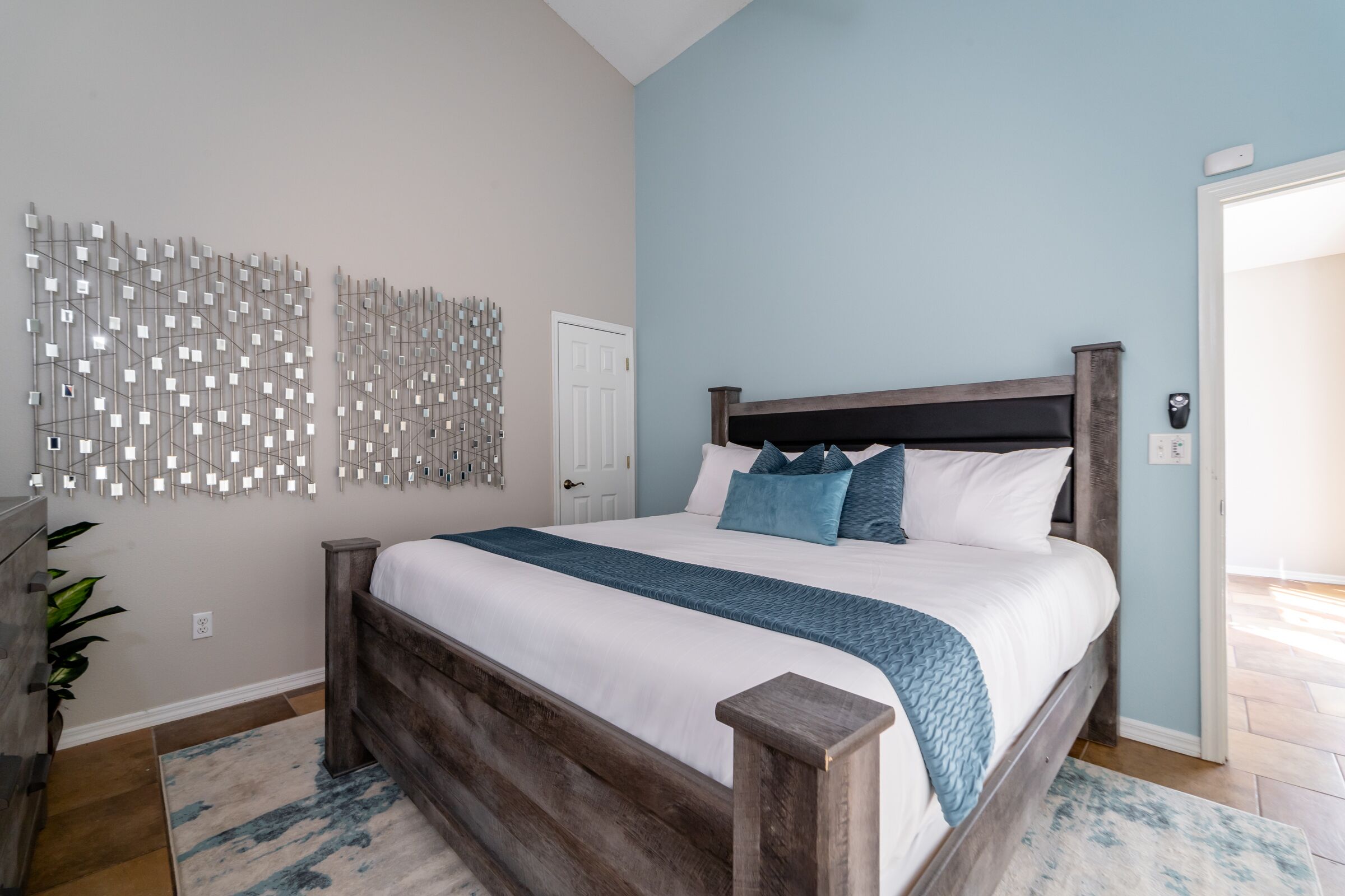 Een slaapkamer met een houten bed, een blauwe accentmuur en een decoratief wandobject.