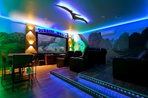 A room with a large flat-screen TV, comfortable seating, and a dinosaur-themed mural.