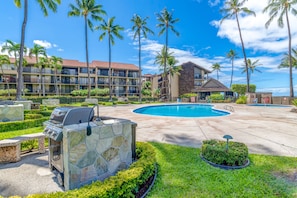 A resort with a swimming pool, palm trees, and a barbecue area.