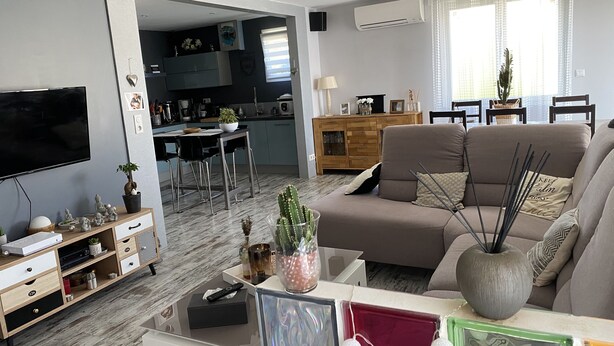 Moderni olohuone, jossa on sohva, televisio ja ruokailutila. Taustalla näkyy keittiö.