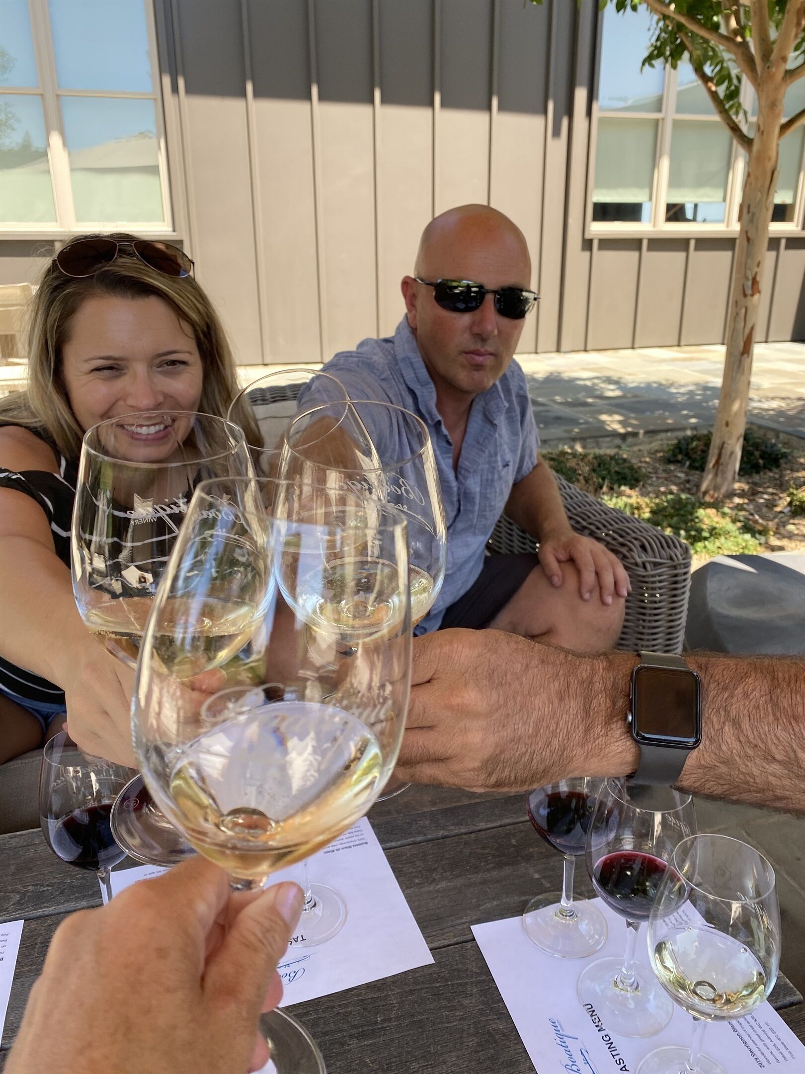 A group of people seated at an outdoor table with wine glasses, a menu, and a smartphone.