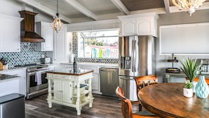 A modern kitchen with white cabinetry, a stainless steel refrigerator, and a wooden dining table. - Lakefront Family Getaway | Dock, Hot Tub, Kings (Lakeport)