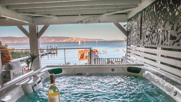 A hot tub with a bottle of wine and glasses, overlooking a marina with boats and a mountainous landscape. - Lakefront Family Getaway | Dock, Hot Tub, Kings (Lakeport)