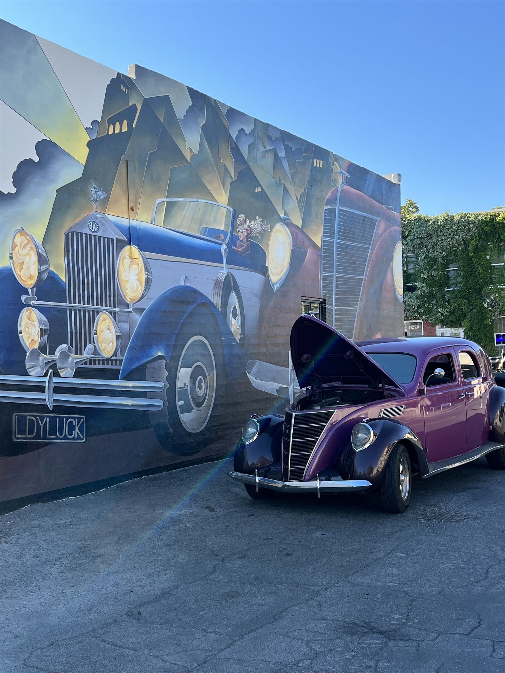 Un coche antiguo estacionado frente a un mural que representa un coche clásico.