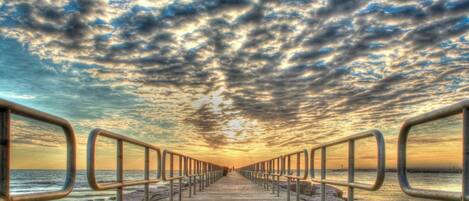 A coastal walkway with metal railings, leading to the sea under a cloudy sky.