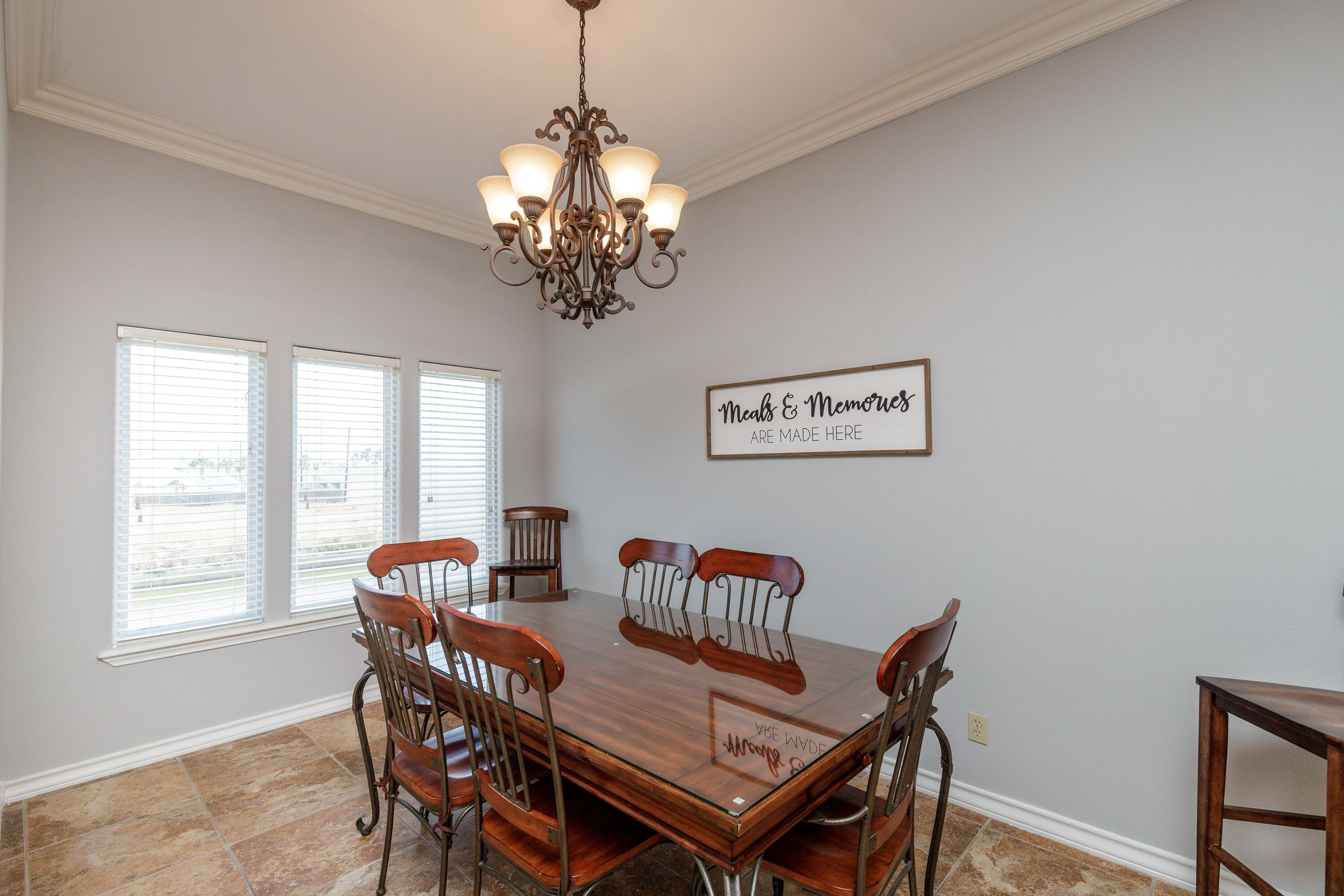 A dining room with a wooden table and chairs, a chandelier, and a sign on the wall.