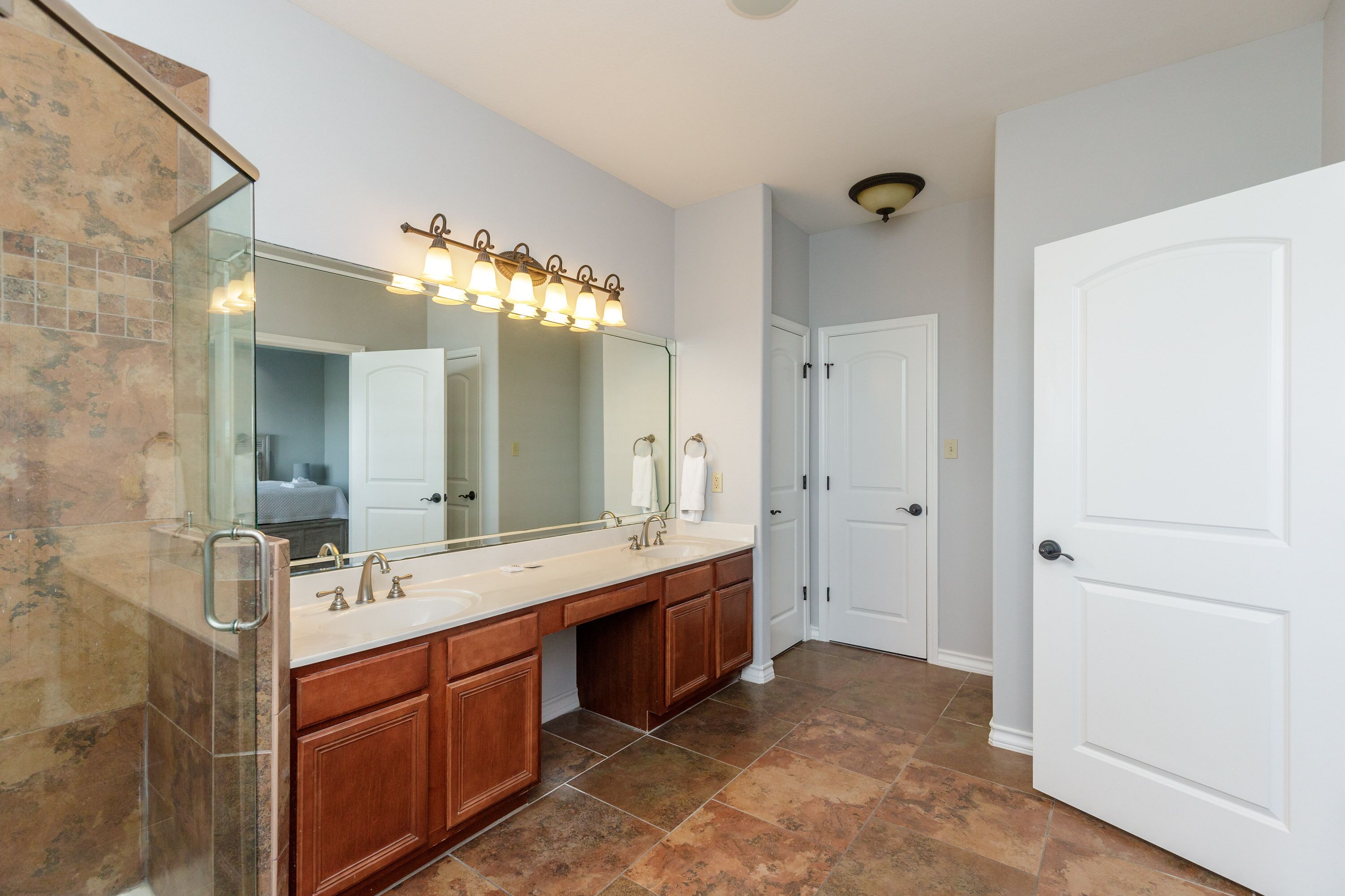A bathroom with a large mirror, double sink vanity, and a shower area.