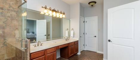 A bathroom with a large mirror, double sink vanity, and a shower area.