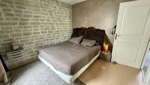 Et soveværelse med stenvæg, en seng med sengegavl, et natbord med lampe og en dør.