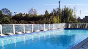 A rectangular swimming pool with clear blue water, surrounded by a white fence and a tiled deck.