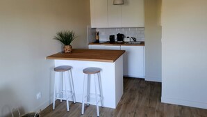 A compact kitchen with a wooden island, two white bar stools, a hanging pendant light, and a potted plant.