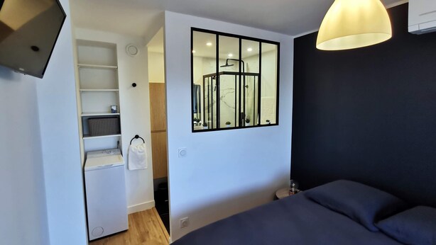 A modern hotel room with a large bed, a wall-mounted TV, a built-in shower, and a small kitchenette.