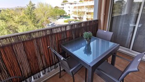 A balcony with a glass table and chairs, a potted plant, and a view of a residential area.