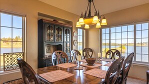 A dining room with a large wooden table, chairs, a chandelier, and a view of a lake through large windows. - On Lake Hatcher! Great Views, Quiet Area, Close to Uptown, New Hot Tub! (Pagosa Springs)