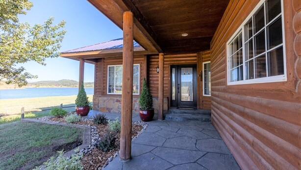 A log cabin with a stone foundation, a covered porch, and a view of a lake. - On Lake Hatcher! Great Views, Quiet Area, Close to Uptown, New Hot Tub! (Pagosa Springs)