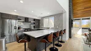 A modern kitchen with a central island, bar stools, and a large window. - Upscale Abode w/Mountain & Golf Course Views•Sleeps 11•BBQ•Steps to Free Shuttle (Park City)