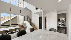 A modern kitchen with a marble countertop, a dining area with chairs, and a staircase leading to an upper level.