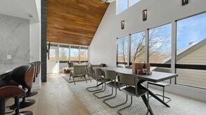 A modern dining area with a high ceiling, large windows, and a view of the outdoors. - Upscale Abode w/Mountain & Golf Course Views•Sleeps 11•BBQ•Steps to Free Shuttle (Park City)