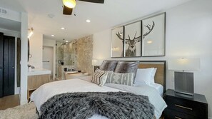 A modern bedroom with a large bed, a nightstand, a TV, and a bathroom with a marble wall and a shower. - Upscale Abode w/Mountain & Golf Course Views•Sleeps 11•BBQ•Steps to Free Shuttle (Park City)