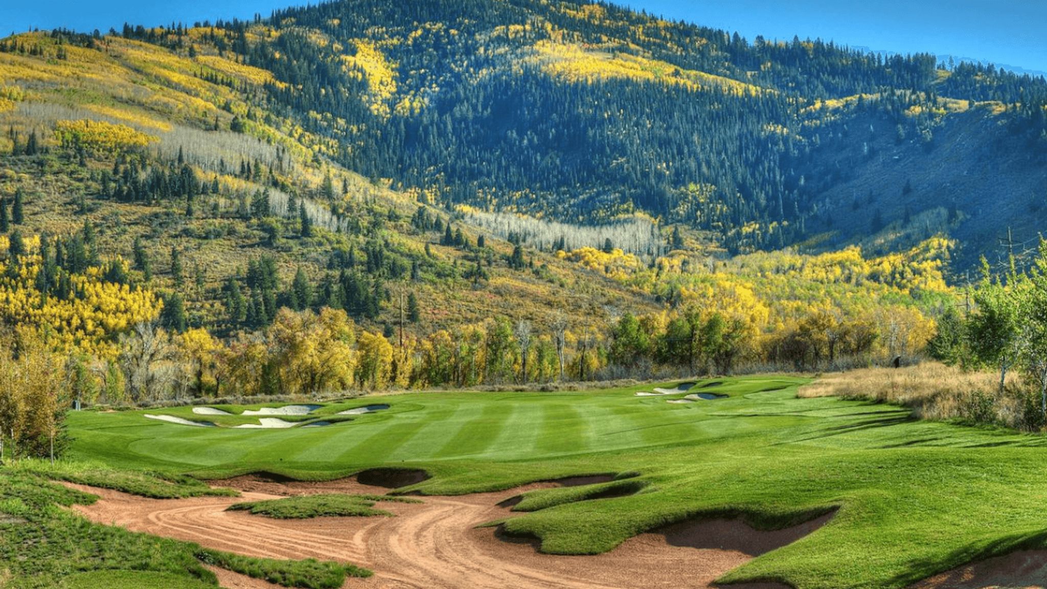 Un campo de golf con un sendero de tierra, fairways verdes y búnkeres de arena.