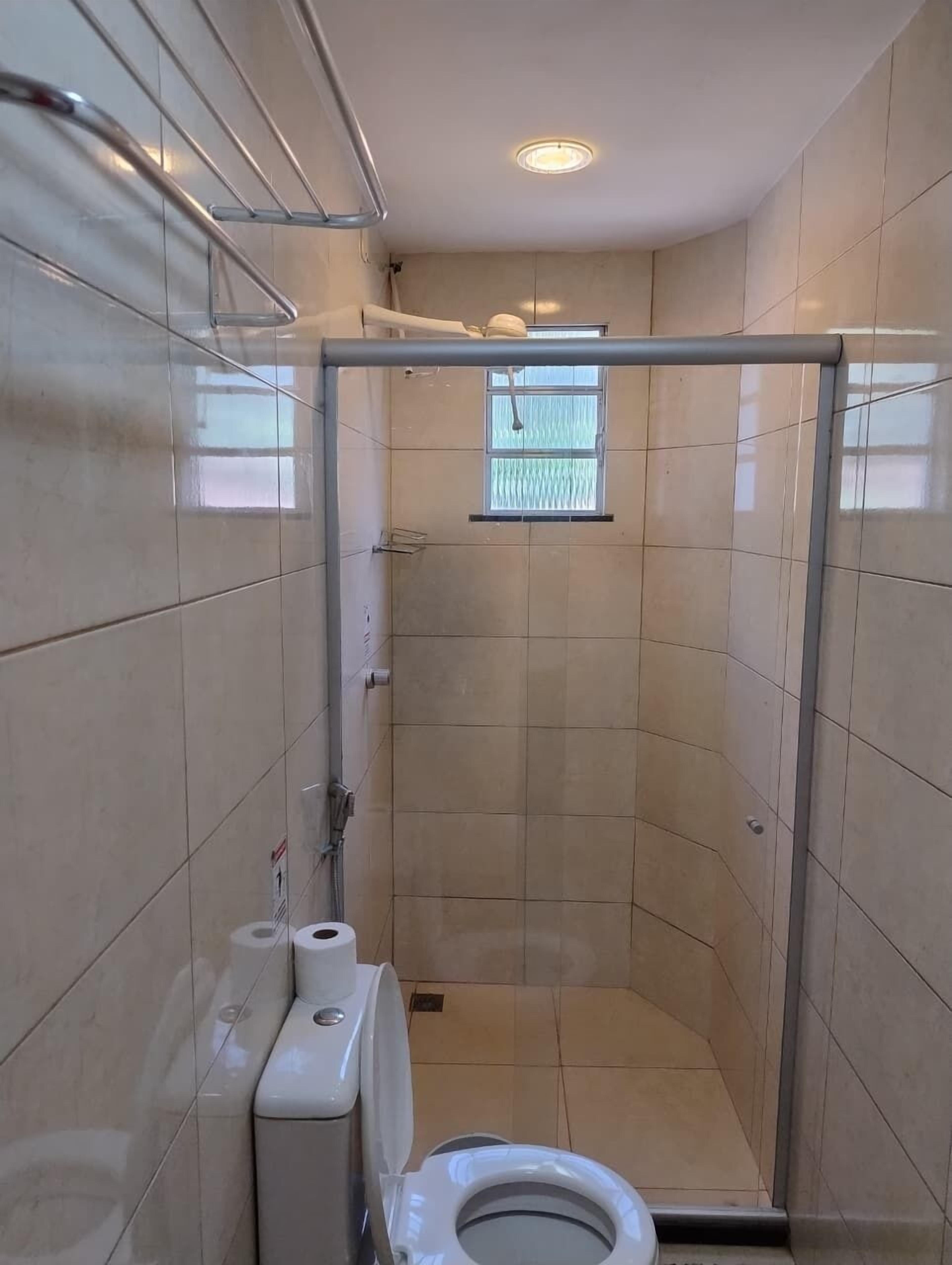 A small, tiled bathroom with a toilet, a hand dryer, and a window.