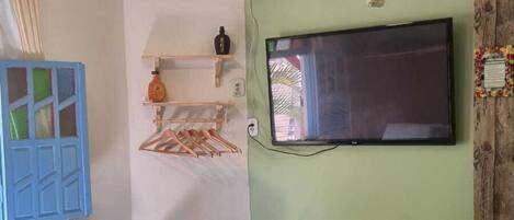 Un dormitorio con una cama, ventilador de techo, aire acondicionado, televisor y estante de madera.