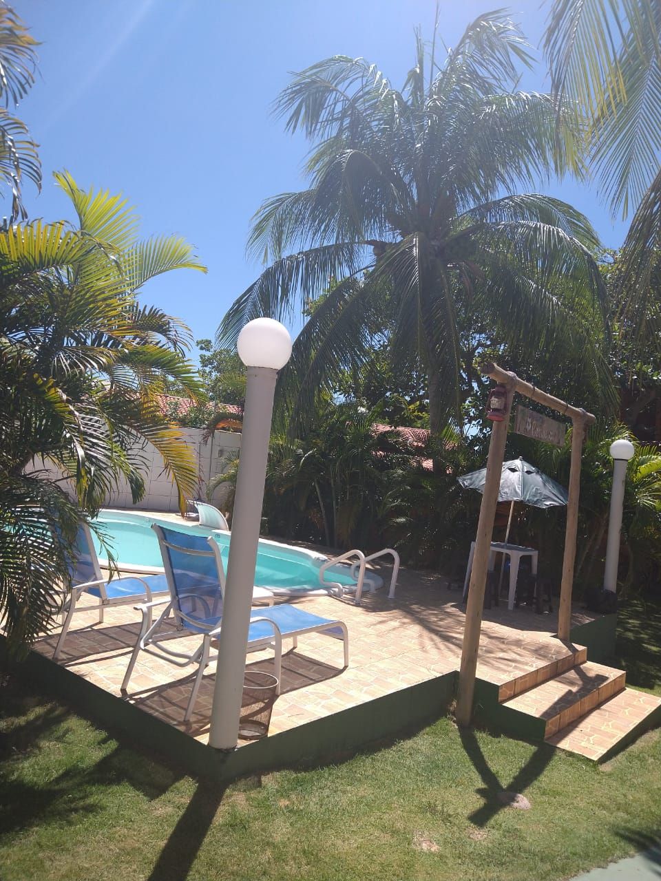 A pool area with lounge chairs, a small table, and a wooden pergola.