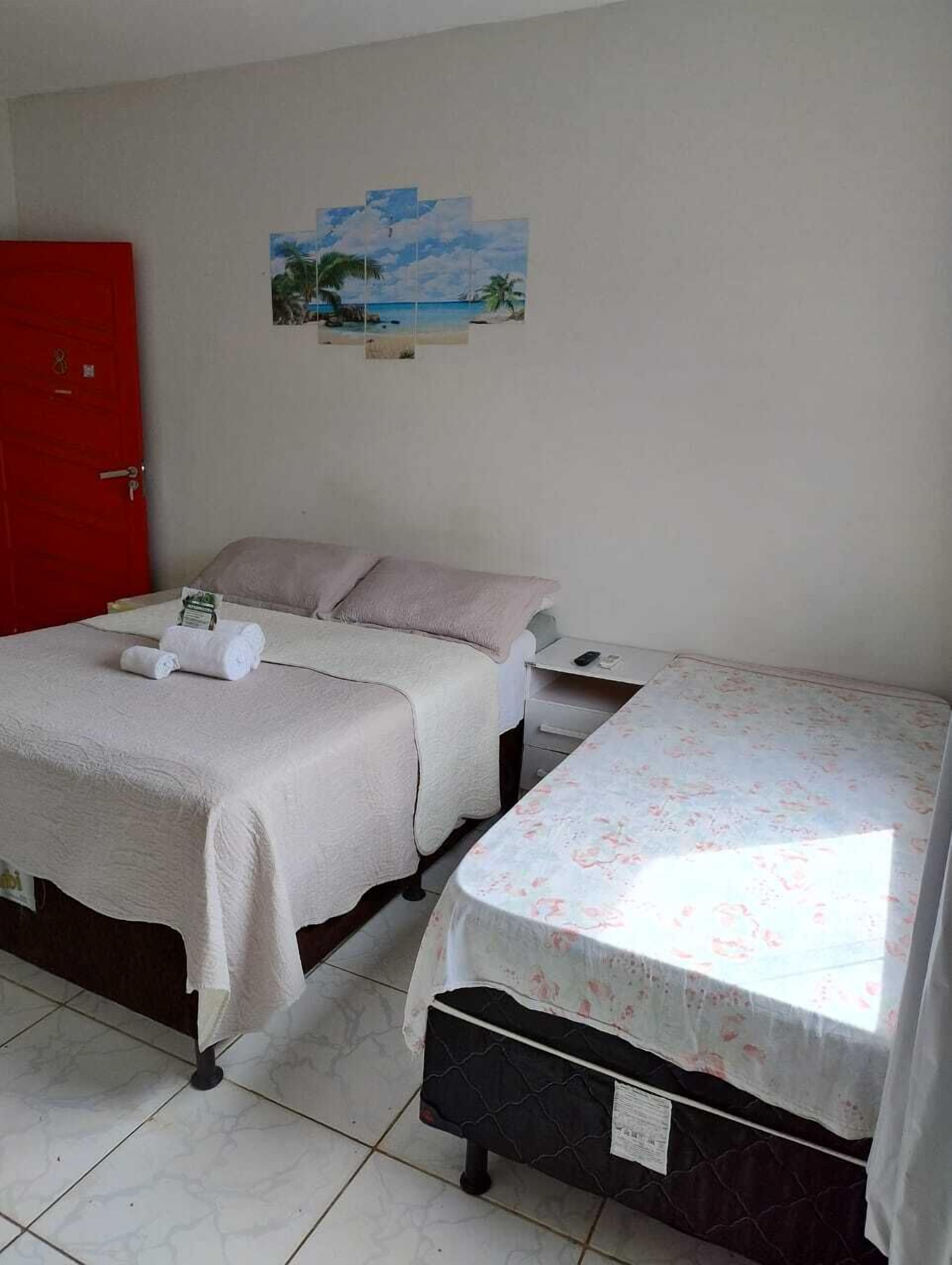 Une chambre avec deux lits, une porte rouge et un tableau sur le mur représentant un paysage de plage.