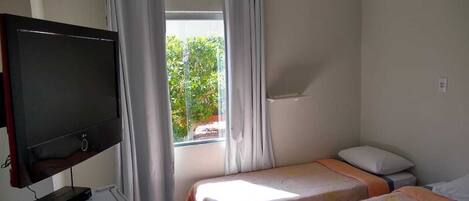 Una habitación pequeña y limpia con dos camas, un televisor y una ventana con cortinas.