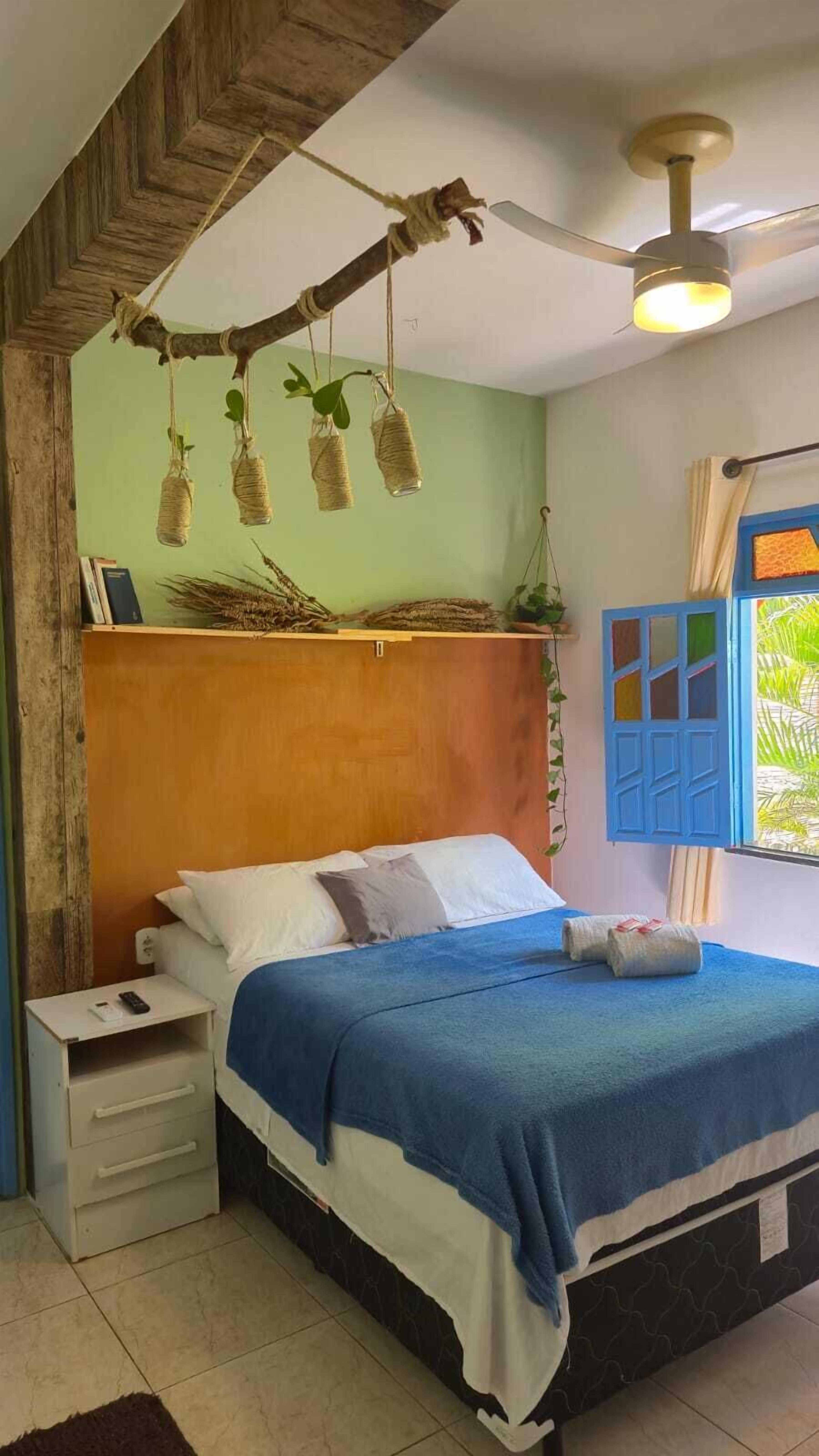 A bedroom with a bed, a nightstand, a ceiling fan, and a window with blue shutters.
