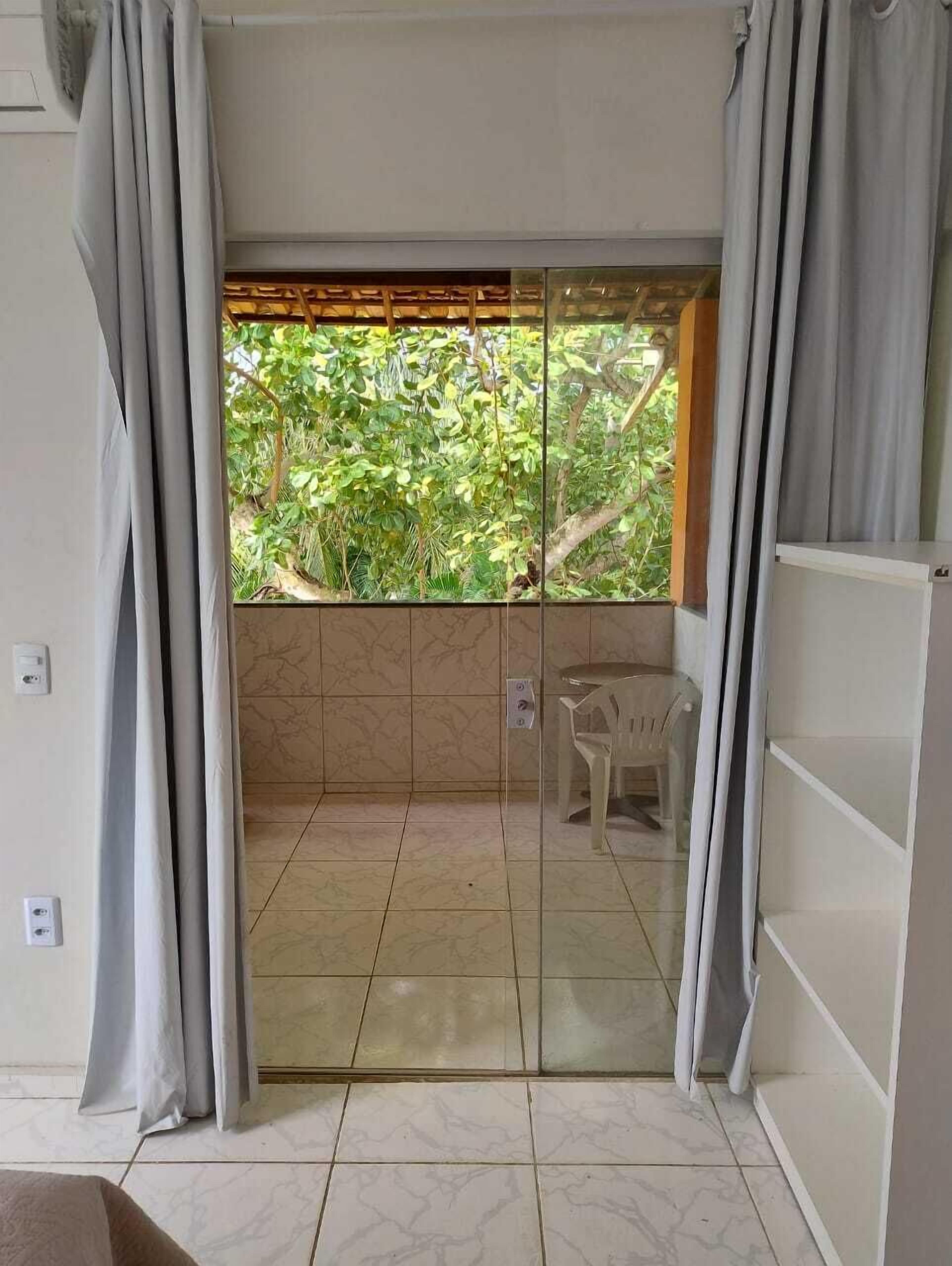 A room with a sliding glass door leading to a balcony with a view of greenery.