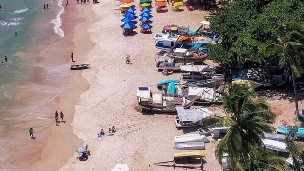 Een strand met rijen kleurrijke parasols, strandstoelen en boten.