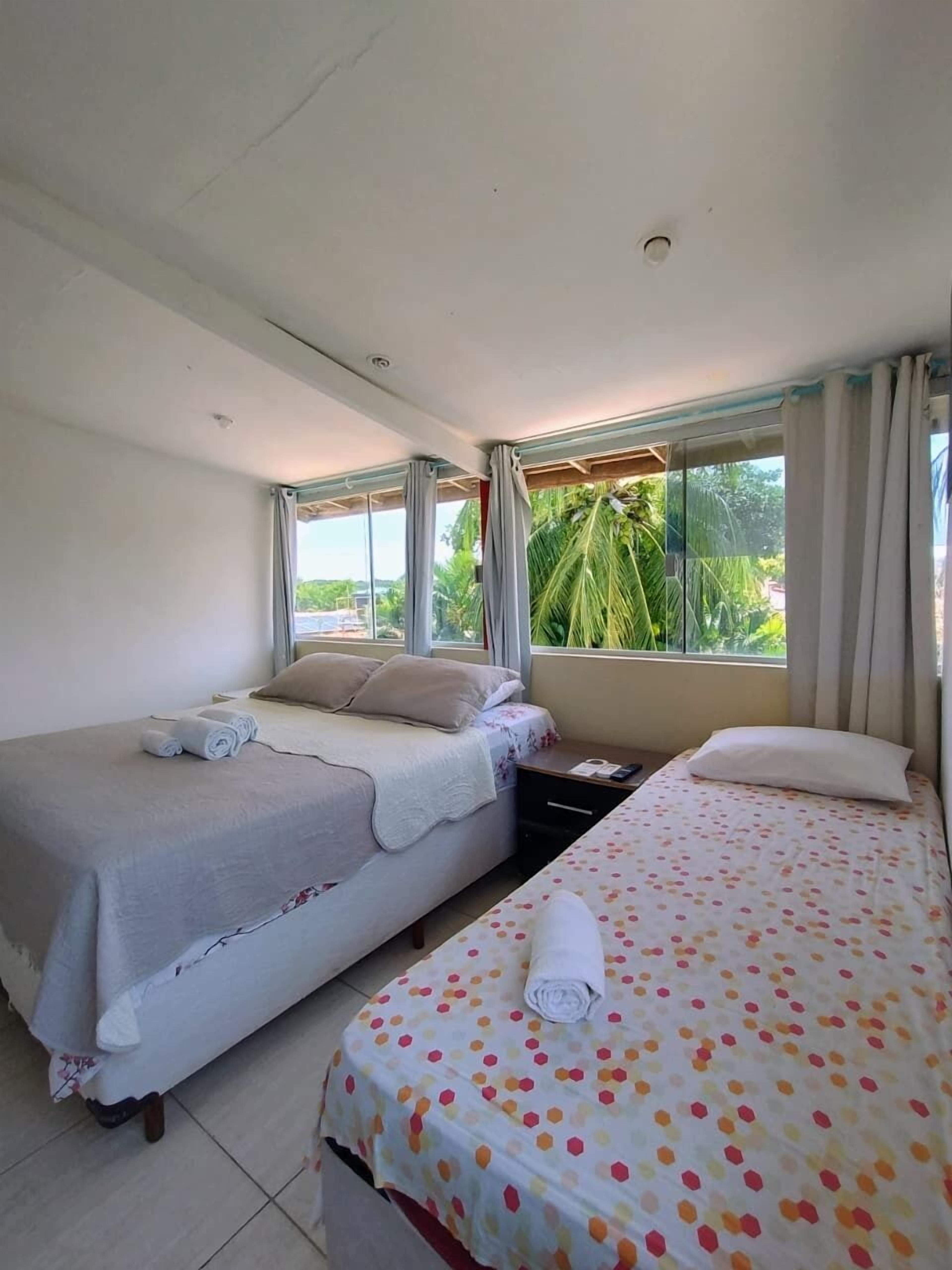 Quarto de hotel com duas camas, mesa de cabeceira e janela com cortinas.