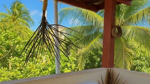 Een kamer met een witte stoel, een kleine tafel, een hangplant en uitzicht op palmbomen.