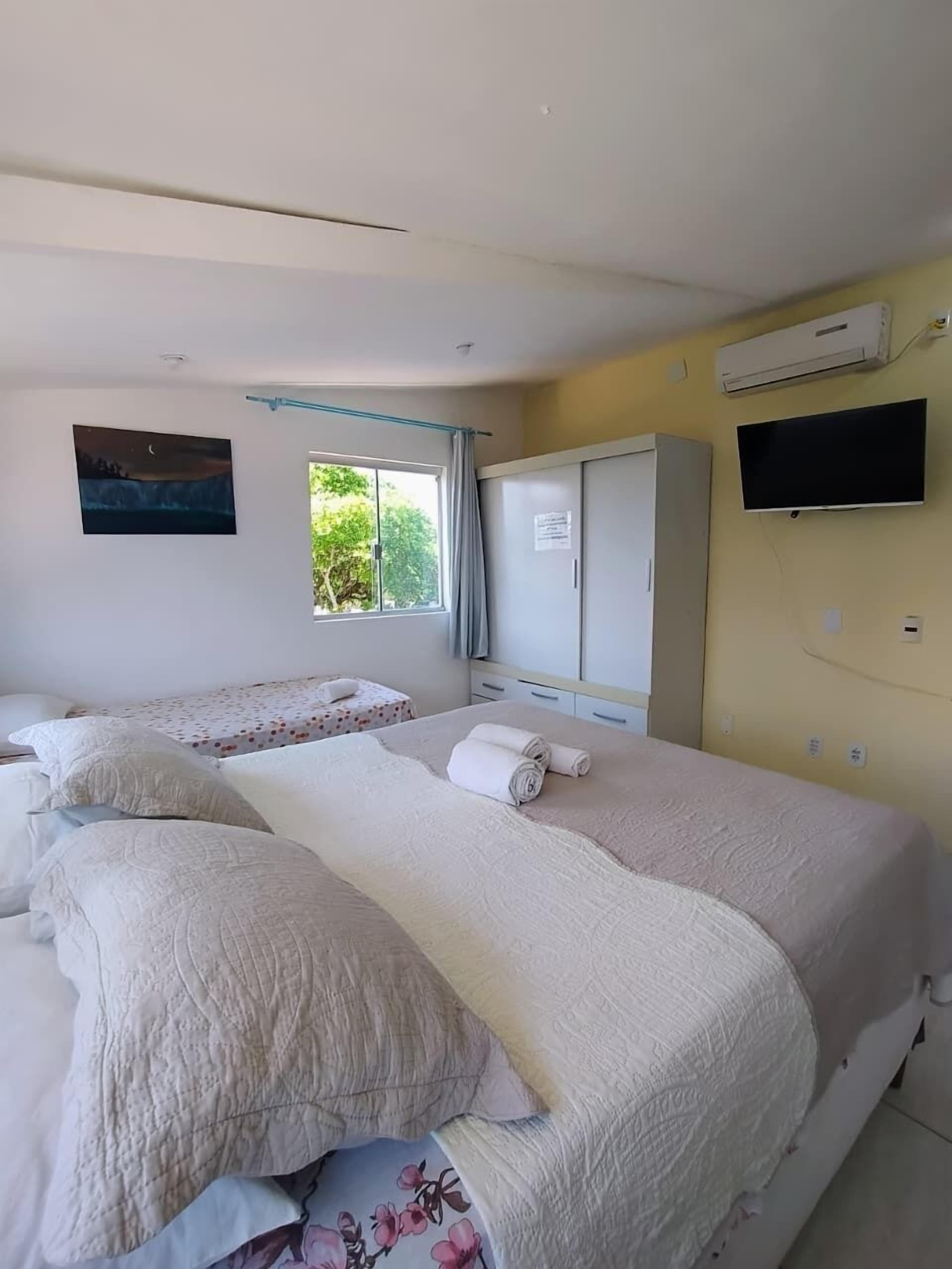 A hotel room with two beds, a wardrobe, a TV, and an air conditioning unit.